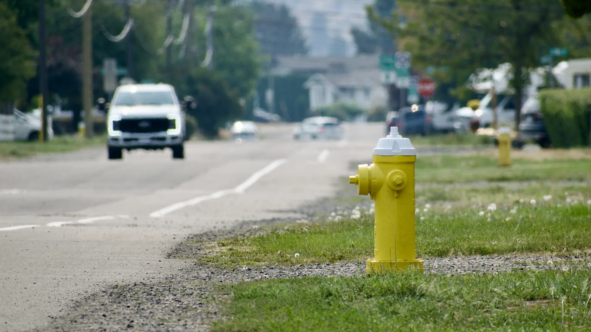 A yellow fire hydrant at the side of the road. In the distance, a truck approaches.